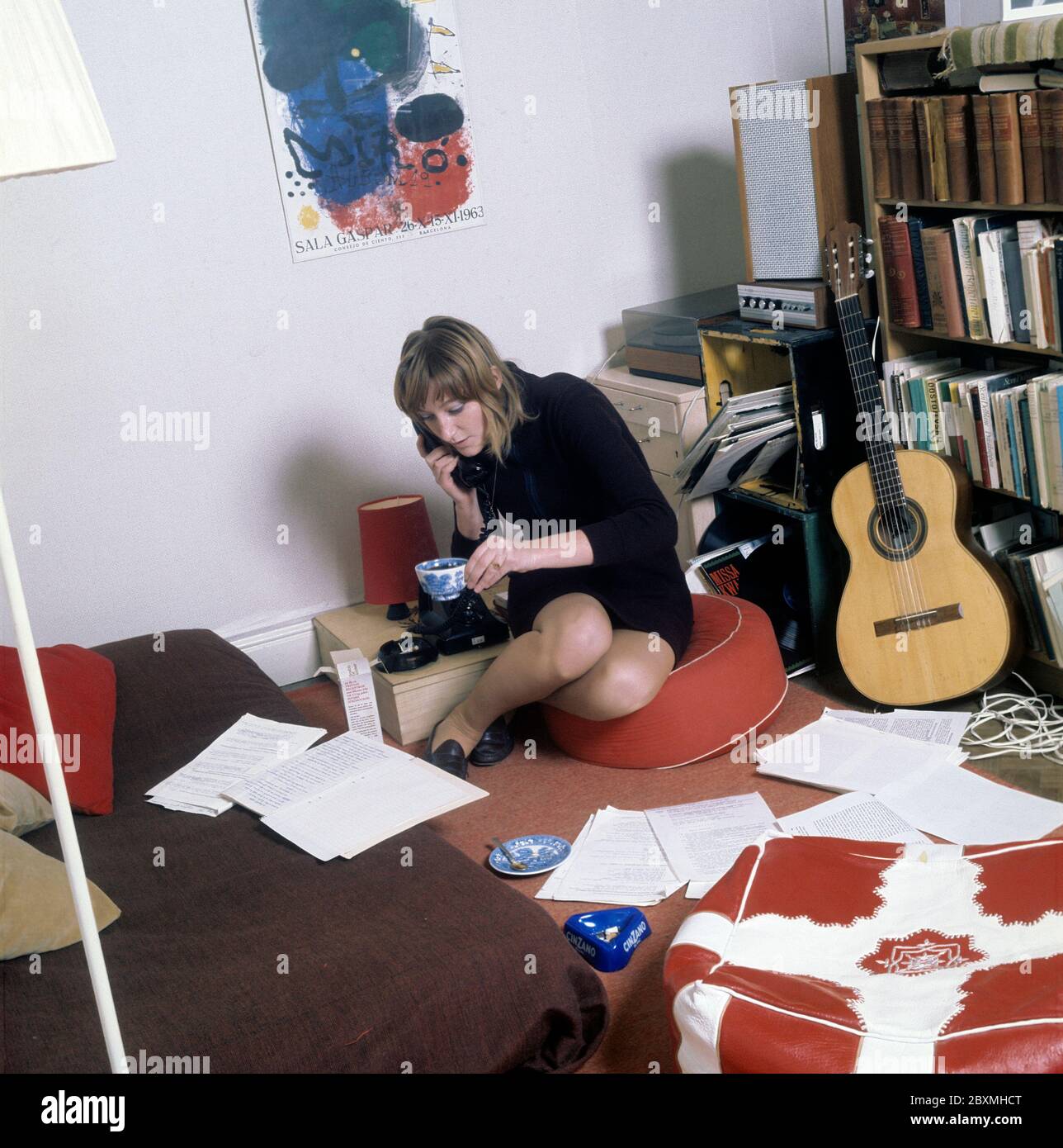 In den 1960er Jahren. Eine junge Frau in ihrer Wohnung. Ein Student zu Hause mit einem Bücherregal voller Bücher und Literatur. Während sie am Telefon telefoniert und eine Zigarette raucht, schaut sie sich einige Dokumente an, die auf dem Boden und dem Bett verteilt sind. Bild aufgenommen im november 21 1968. Kristoffersson Ref. CV51-2 Stockfoto