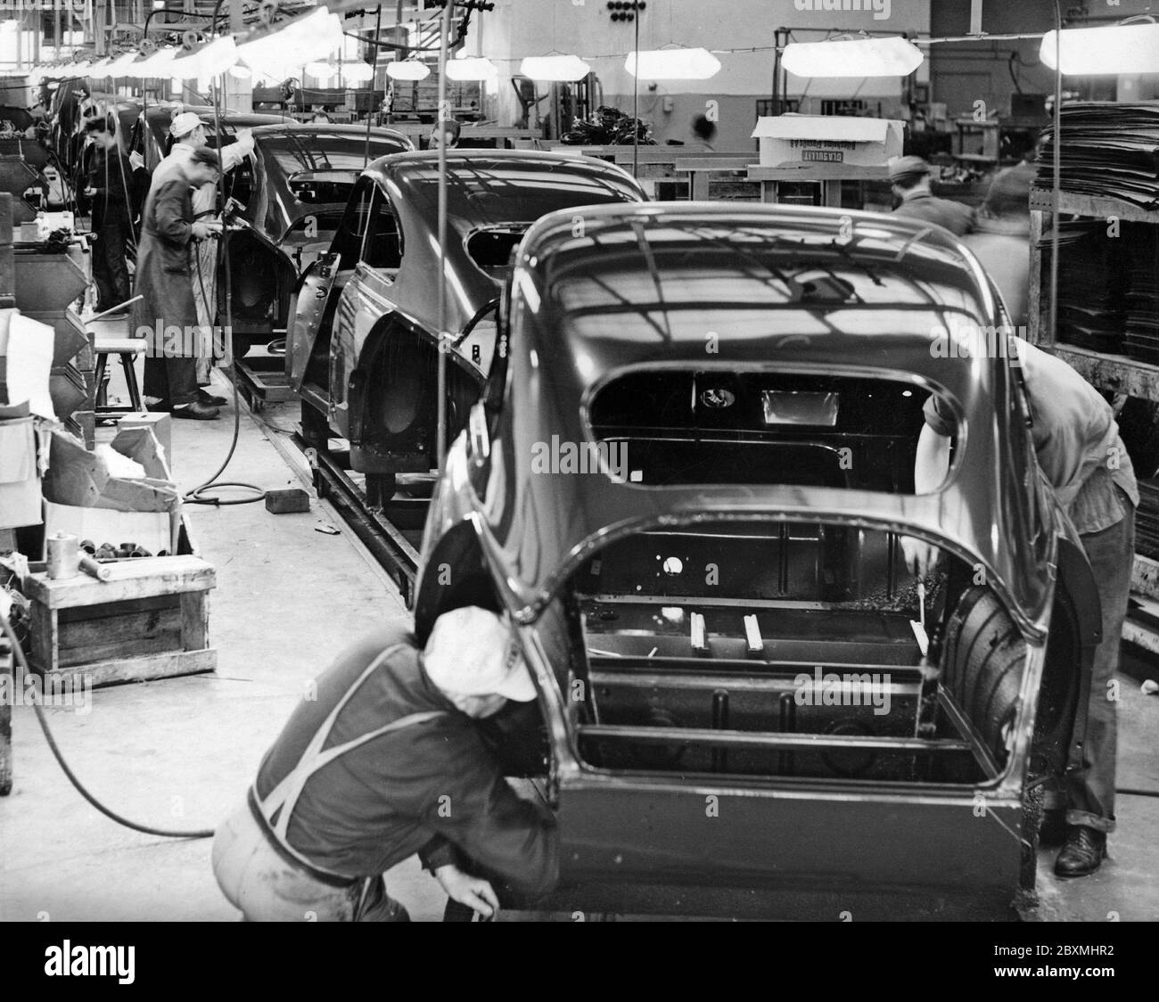 Automobilbau in den 1950er Jahren. Die Saab Autofabrik in Trollhättan Schweden mit ihrer Produktionslinie. Arbeiter an einer Montagelinie fügen Teile hinzu, während die Karosserien von Arbeitsplatz zu Arbeitsplatz wechseln, bis die Endmontage hergestellt ist. Das Modell ist Saab 93. Ein Dreizylinder-Zweitaktmotor mit 33 ps. Stockfoto