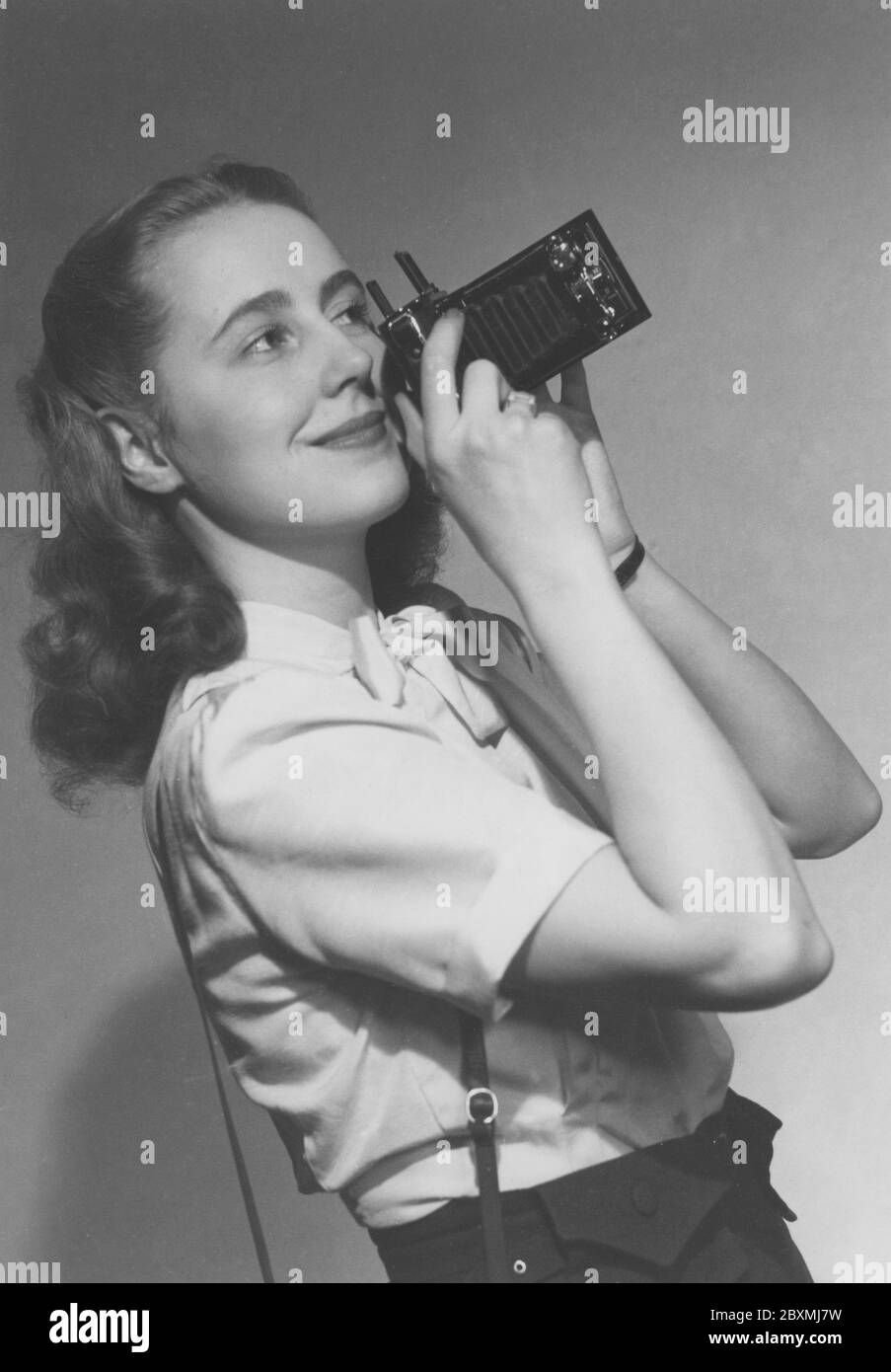 Amateurfotograf in den 1940er Jahren. Eine junge Frau fotografiert an einem Sommertag. Das Kameramodell ist praktisch. Wenn Sie es nicht verwenden, werden die Linse und der Balg in das Kameragehäuse gefaltet. Um Bilder aufzunehmen, haben Sie es geöffnet und waren bereit zu gehen. Die Kamera produzierte analogen Film. Margareta von Törne ist beim Fotografieren abgebildet und die Fotografie wurde ursprünglich auf dem Cover eines Buches mit dem Titel Handbuch für den Amateurfotografen 1948 verwendet. Stockfoto