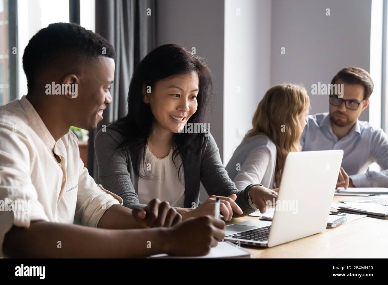 Multiethnische jüngere ältere Partner arbeiten an Aufgabe mit Laptop zusammen Stockfoto