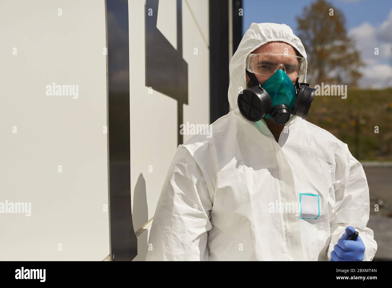 Taille oben Porträt von männlichen Arbeiter tragen Hasmat Anzug im Freien durch Gebäude in Sonnenlicht während der Desinfektion oder Reinigung, kopieren Raum stehen Stockfoto