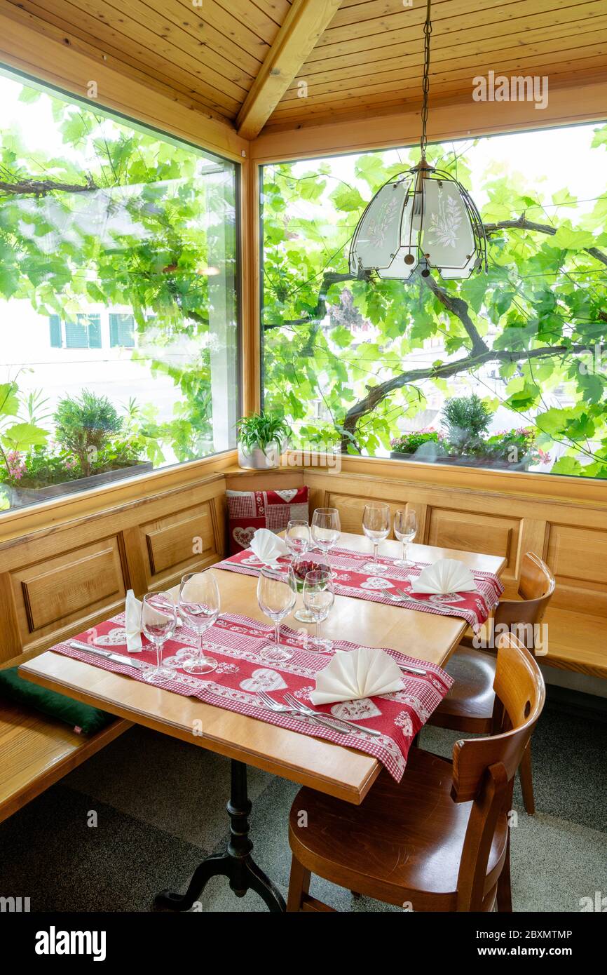 Ein charmanter und einladender Restauranttisch mit Erkerfenster und Weinreben dahinter mit farbenfrohen Platzeinstellungen Stockfoto