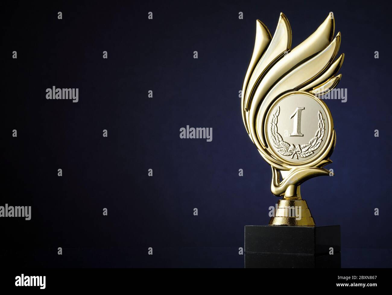 Gewinner Goldtrophäe mit gravierter Medaillon mit Nummer 1 und Lorbeerkranz umgeben von einem Wirbel über einem dunkelblauen Hintergrund mit Copyspace für einen cha Stockfoto