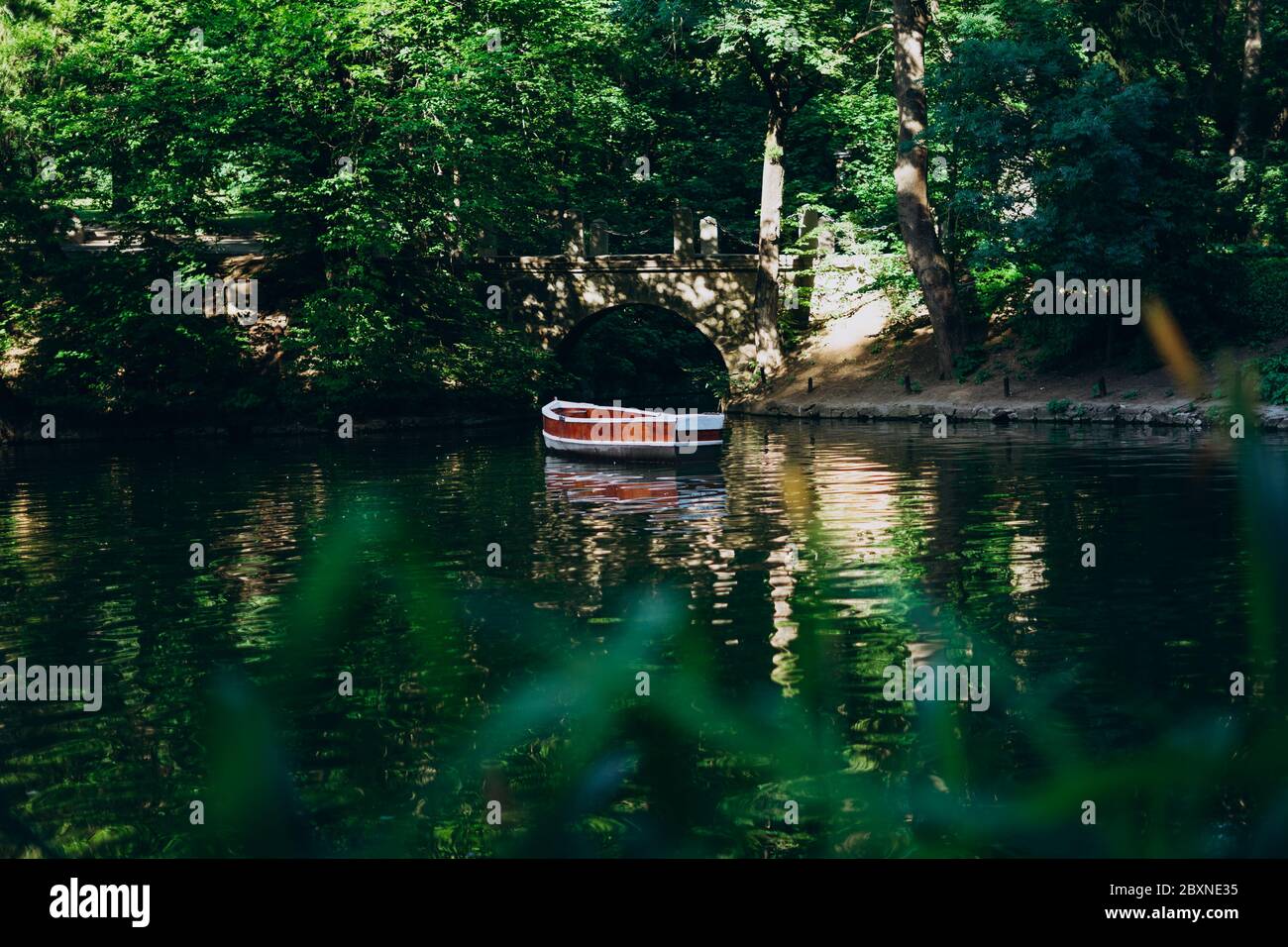 Uman, Ukraine. Rotes Boot auf dem See unter hohen Bäumen. Malerischer See im Wald mit einem hölzernen Shuttle. Nationalpark mit hohen grünen Bäumen, See Stockfoto
