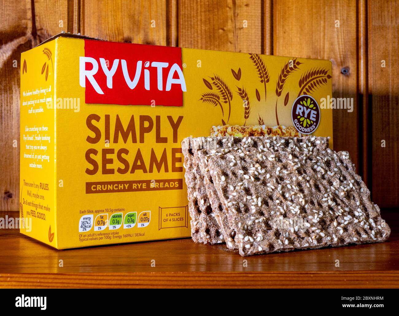 Eine Schachtel Ryvita ‘simpliziert Sesam’ knusprige Roggenbrote, mit vier der hochfaserigen knusprigen Brote, die sich gegen die Schachtel lehnen, auf einem Regal in einem Kiefernschrank. Stockfoto