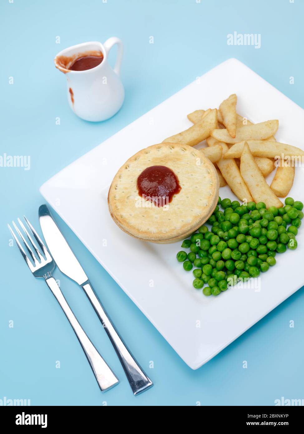 Eine australische Fleischpastete serviert mit Erbsen und Pommes frites vor einem blauen Hintergrund isoliert Stockfoto