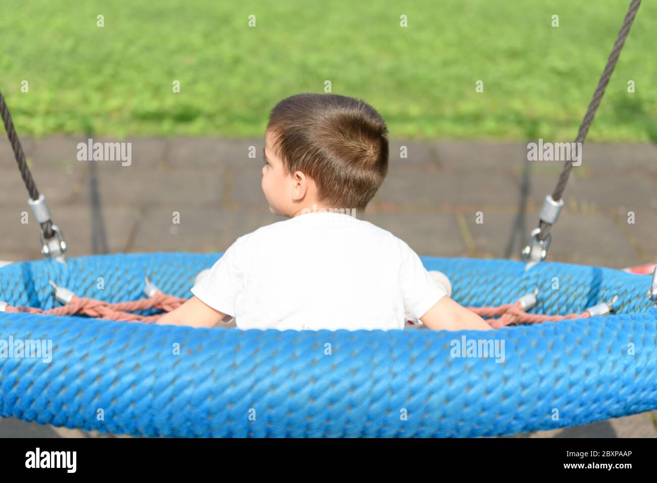 Junge schwingt tagsüber auf dem Spielplatz Stockfoto