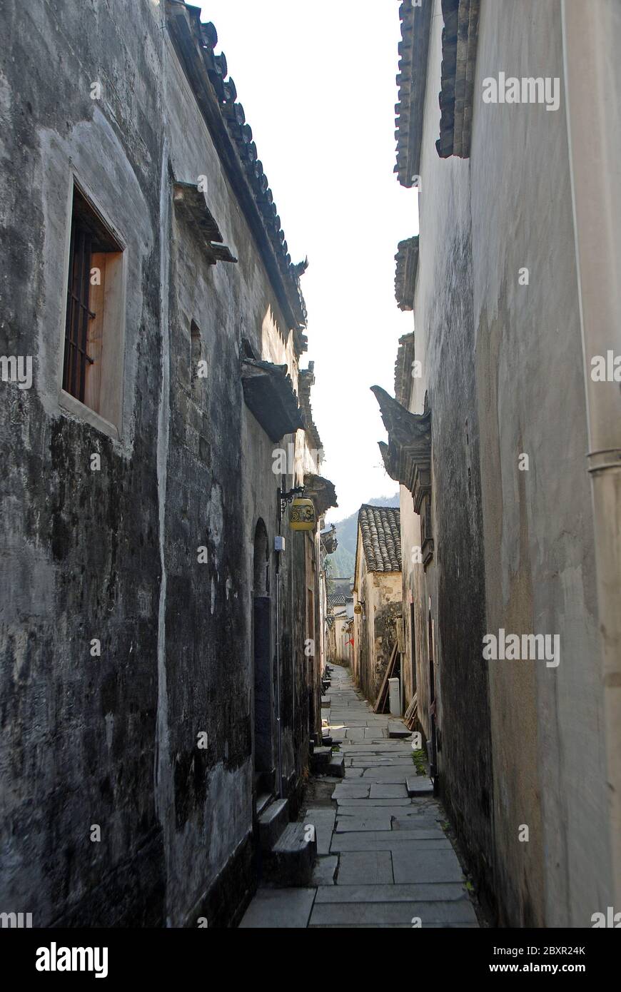 Die alte Stadt Xidi in der Provinz Anhui, China. Eine schmale Hinterstraße in der Altstadt von Xidi mit historischen Gebäuden, Steinweg und dunklen Mauern Stockfoto