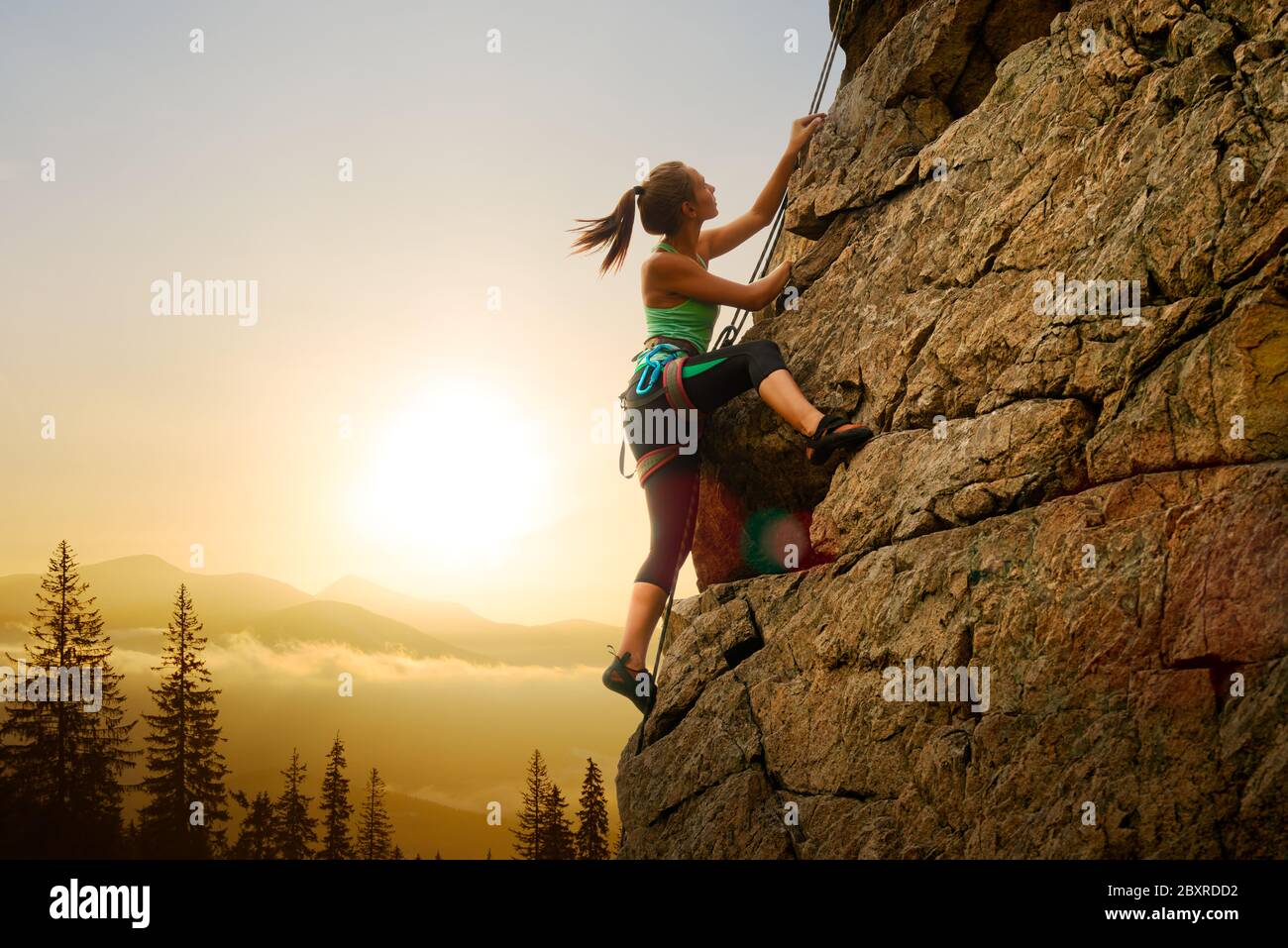 Schöne Frau Klettern auf dem High Rock bei Foggy Sonnenuntergang in den Bergen. Adventure und Extreme Sport Konzept Stockfoto