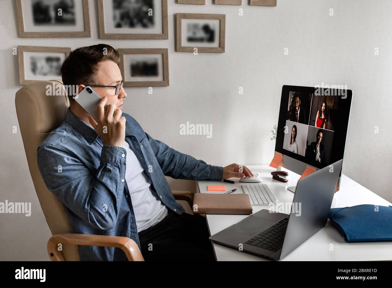 Junger Mann, der von zu Hause aus Papierkram macht, während er Laptop benutzt und das Telefon in der Hand hält. Stockfoto