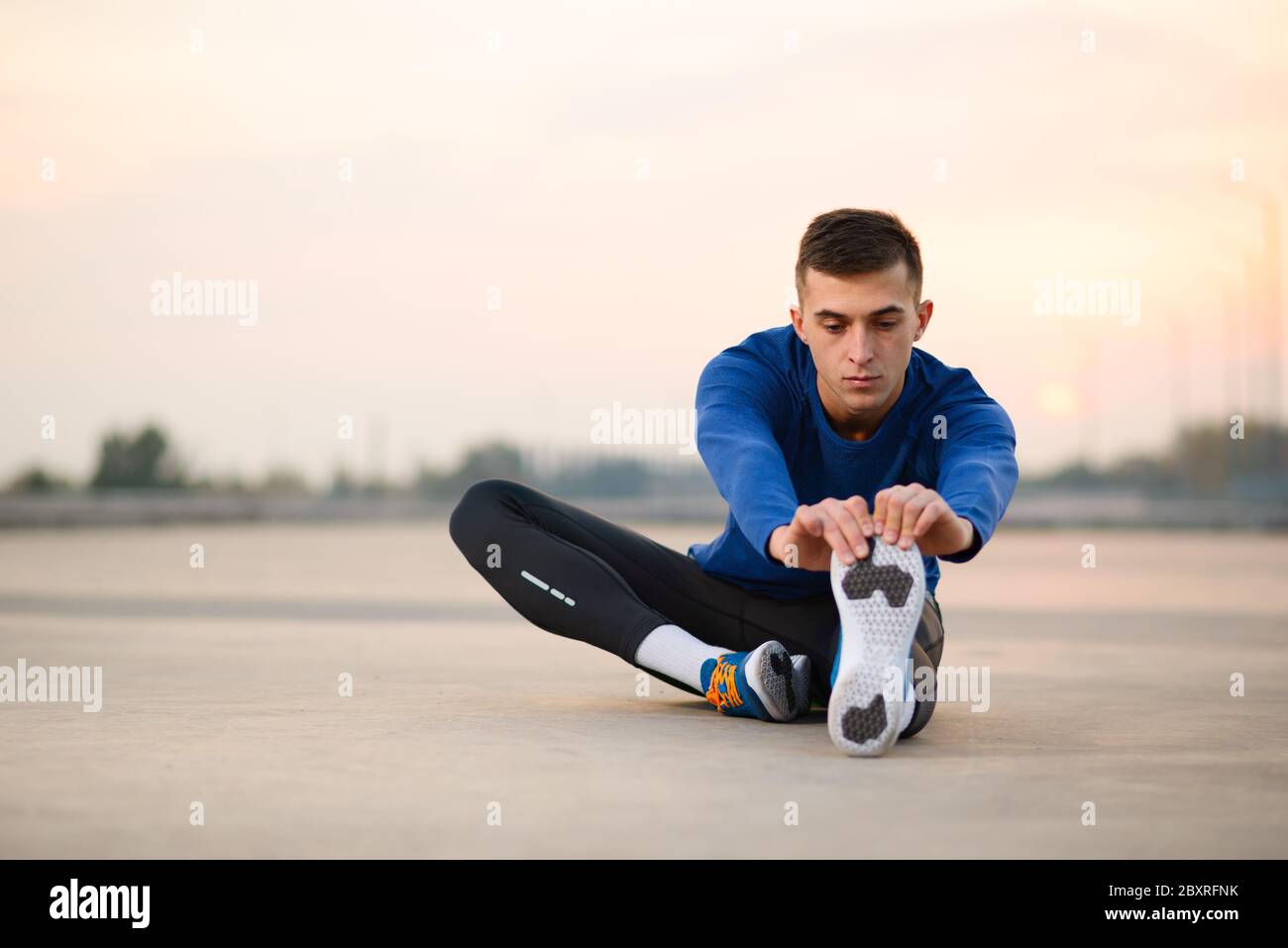 Junger männlicher Läufer Stretching und Vorbereitung für Runat Sonnenuntergang. Gesunder Lebensstil und Active Sport Konzept. Stockfoto