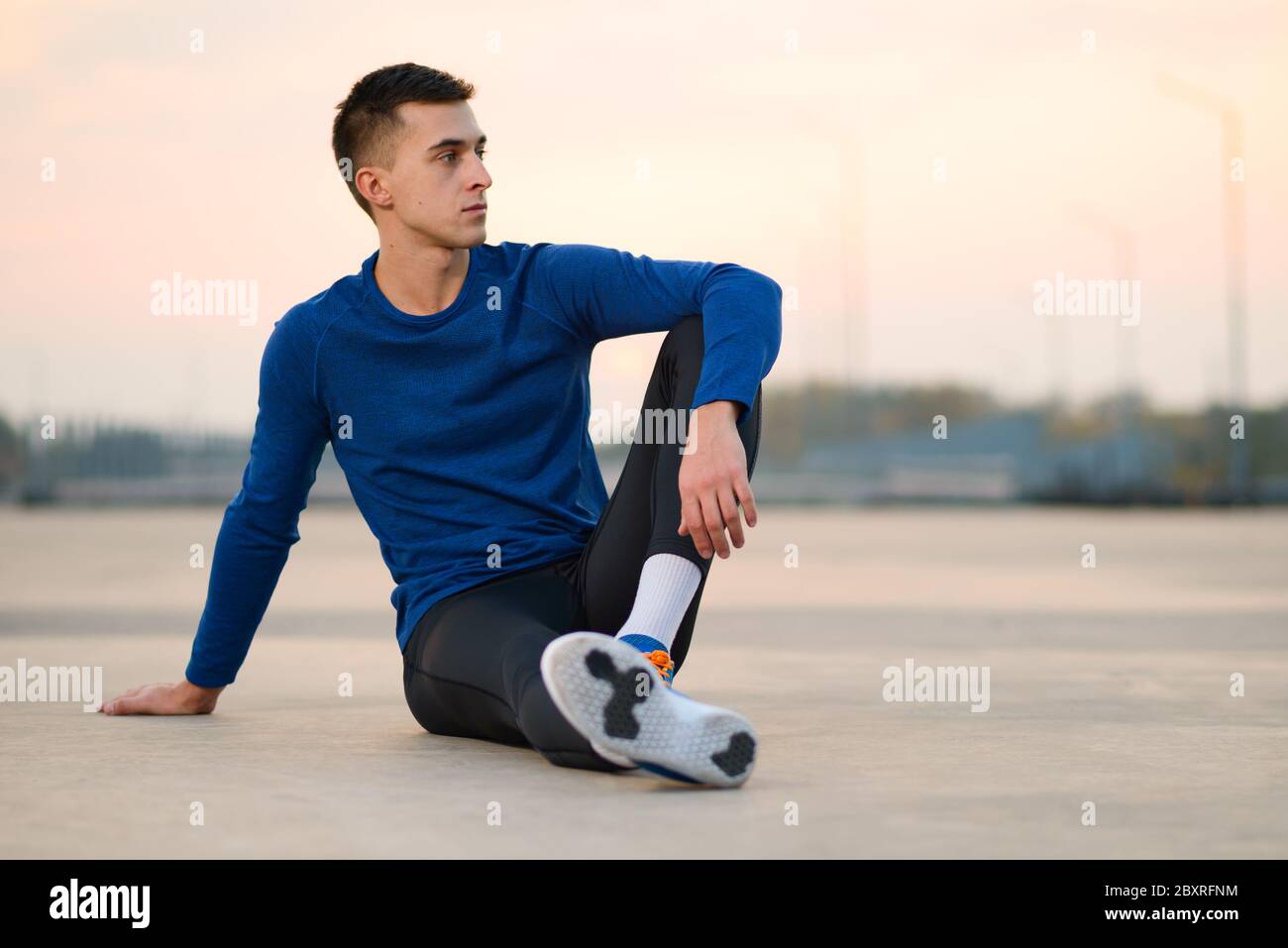 Junger männlicher Läufer, der sich nach dem Lauf bei Sonnenuntergang ausruhte. Gesunder Lebensstil und Active Sport Konzept. Stockfoto