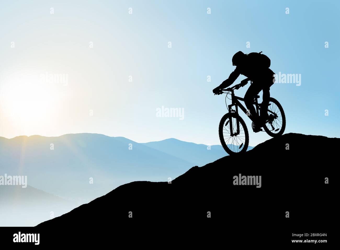 Silhouette von Radler mit dem Fahrrad in den schönen Bergen auf dem Felsen auf dem Sonnenaufgang Himmel Hintergrund. Extreme Sport und Enduro Biking Konzept. Stockfoto