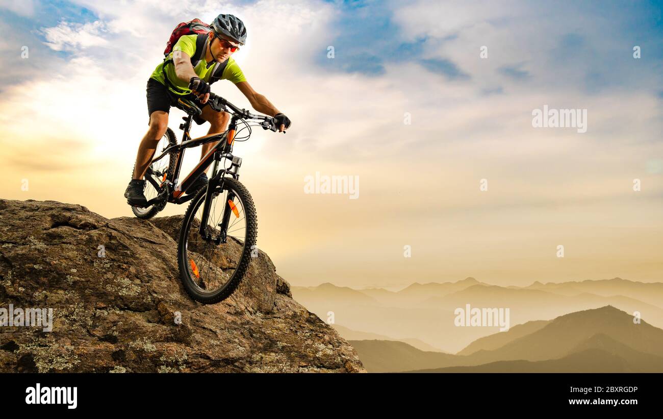 Radler mit dem Fahrrad den Felsen hinunter bei Sonnenaufgang in den schönen Bergen im Hintergrund. Extreme Sport und Enduro Biking Konzept. Stockfoto