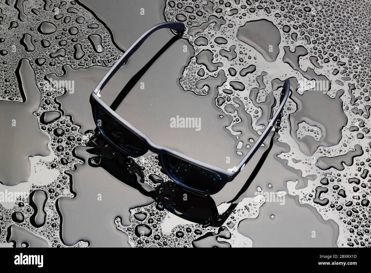 Sonnenbrille auf einer schwarzen nassen Oberfläche mit Wasser Stockfoto