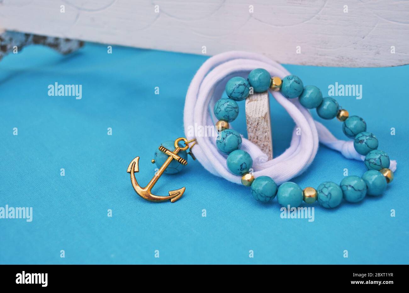 Sommerschmuck - türkisfarbenes Edelsteinarmband und goldener Anker-Charme Stockfoto