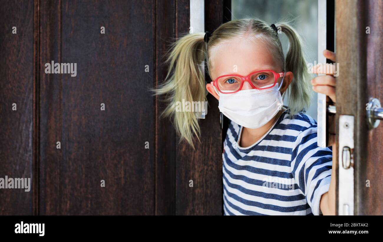 Kleines Kind, das nach dem Aufenthalt zu Hause aus der Tür aufschaute, da es auf der Straße verboten war. Kind trägt medizinische Gesichtsmasken gehen für außerhalb gehen. Stockfoto