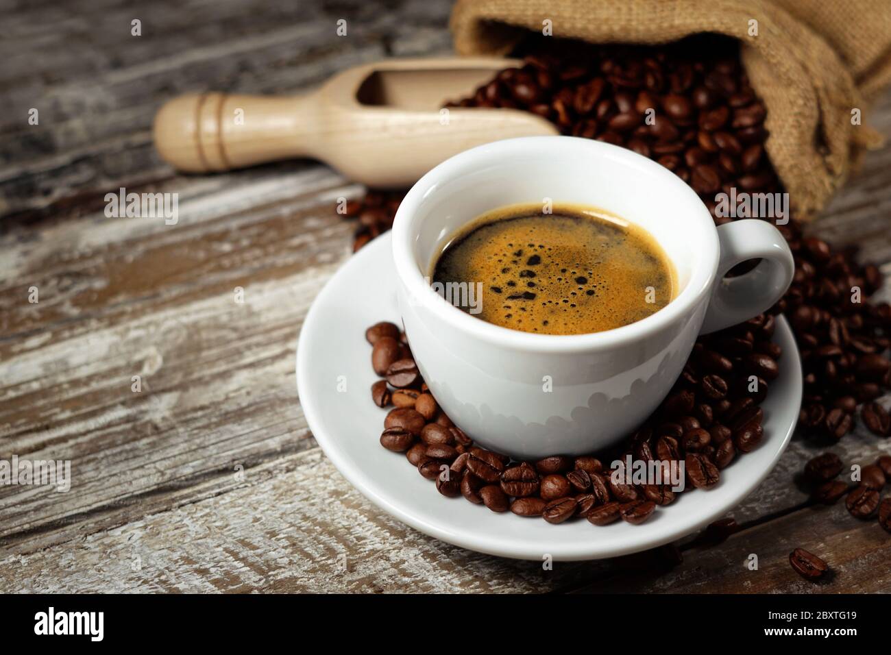 Kaffeetasse und geröstete Kaffeebohnen in einem Sackleinen auf einem rustikalen Holztisch Nahaufnahme auf rostigen Vintage-Hintergrund. Stockfoto