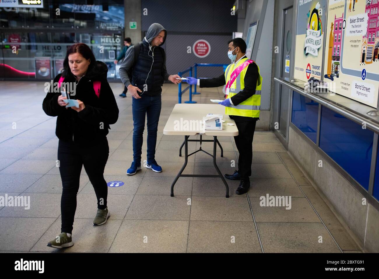 Ein TFL-Mitarbeiter gibt während der Hauptverkehrszeit am ersten Tag des Programms kostenlose Gesichtsmasken und Handschuhe an die Passagiere am Canning Town Station aus. TFL sind Pilotprojekt Stockfoto