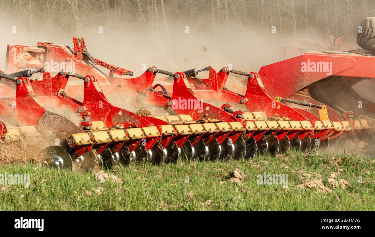 Die landwirtschaftliche Ausrüstung zerschneidet das gepflügte Land. Ein Raupentraktor zieht eine Egge, um den Boden aus nächster Nähe zu lockern. Stockfoto
