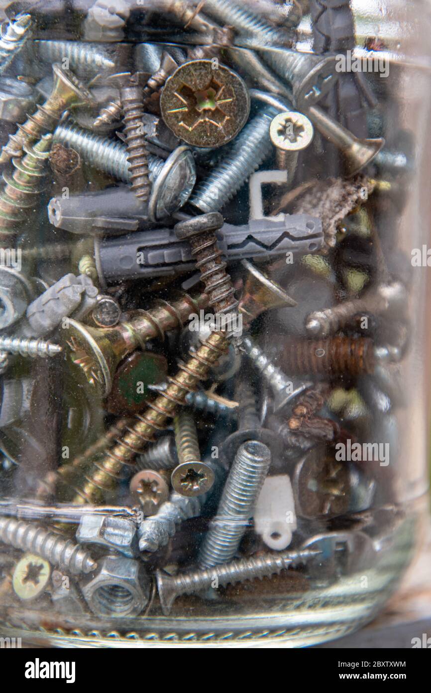 Unschärfe-Nahaufnahme durch verschwommenes dünnes Glas mit alten Metallschrauben, Muttern, Unterlegscheiben und Dübel aufgenommen. Grunge Metallbefestigungen mit verschwommenen Kanten o Stockfoto