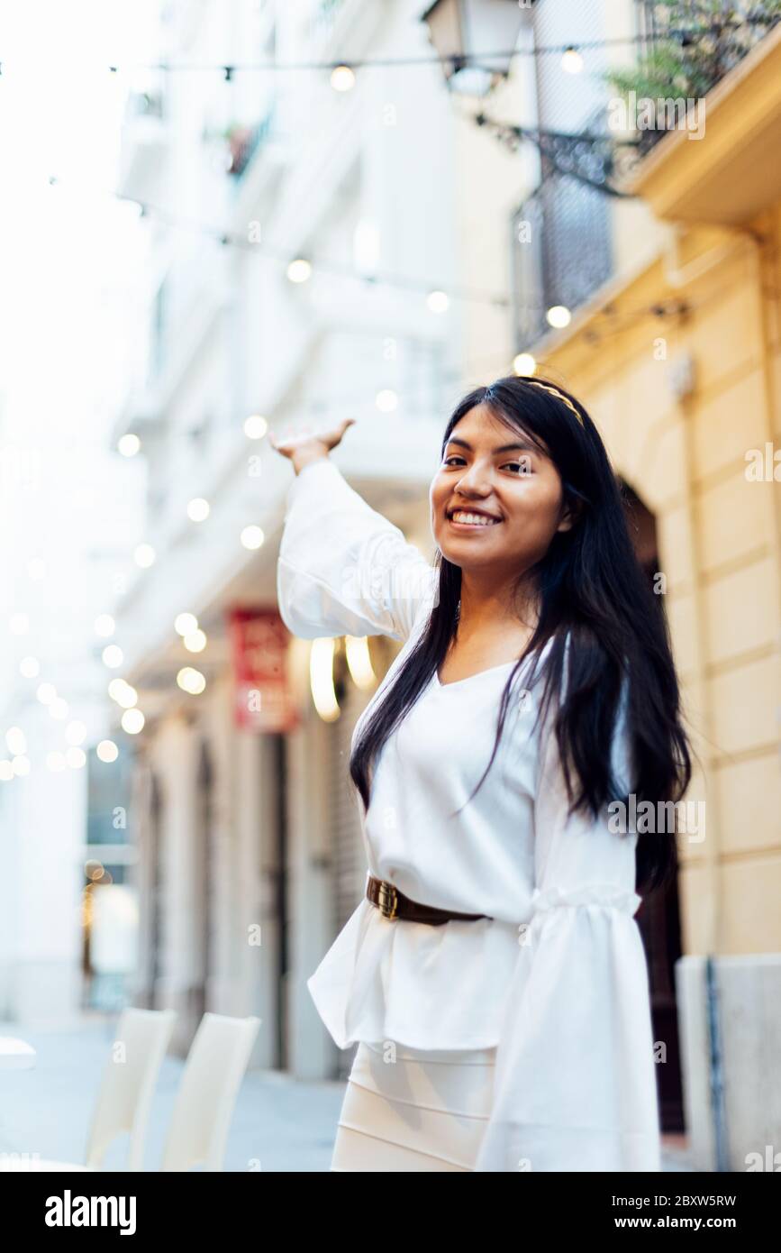 Lateinische Frau mit langen schwarzen Haaren lächelnd auf die Kamera und mit der Hand auf Lichter auf den Straßen. Städtisches Tourismus Konzept Stockfoto