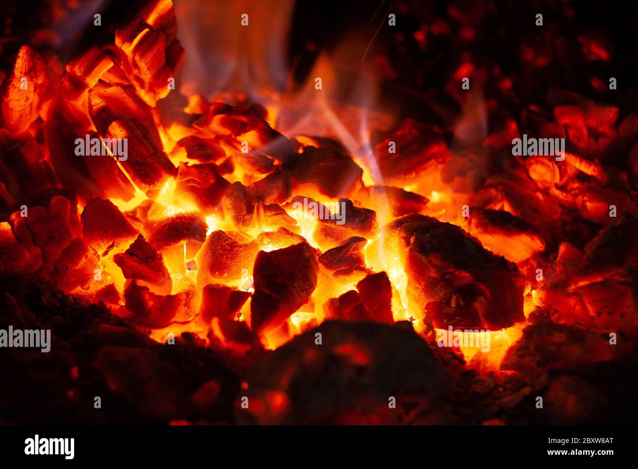 Glühende Glut in glühender roter Farbe, abstrakter Hintergrund. Die heiße Glut brennenden Holzes logs Feuer. Brennholz auf dem Grill. Textur von Feuer Brennstoff Briquet Stockfoto