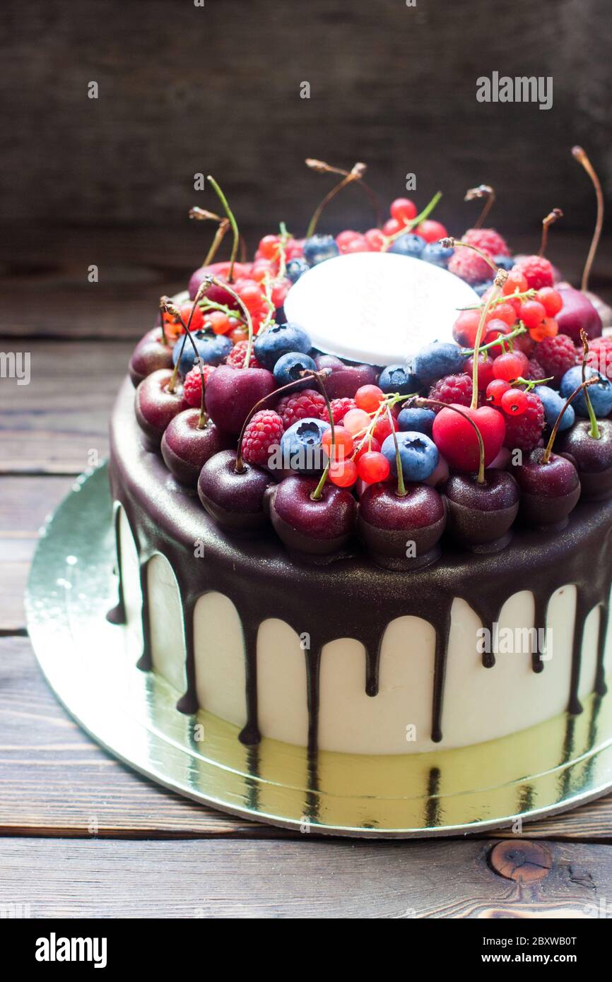 Geburtstagskuchen mit geschmolzener Schokolade, frischer Kirsche, Himbeere, Erdbeere, rote Johannisbeere, Heidelbeere auf rustikalem Holzhintergrund. Stockfoto