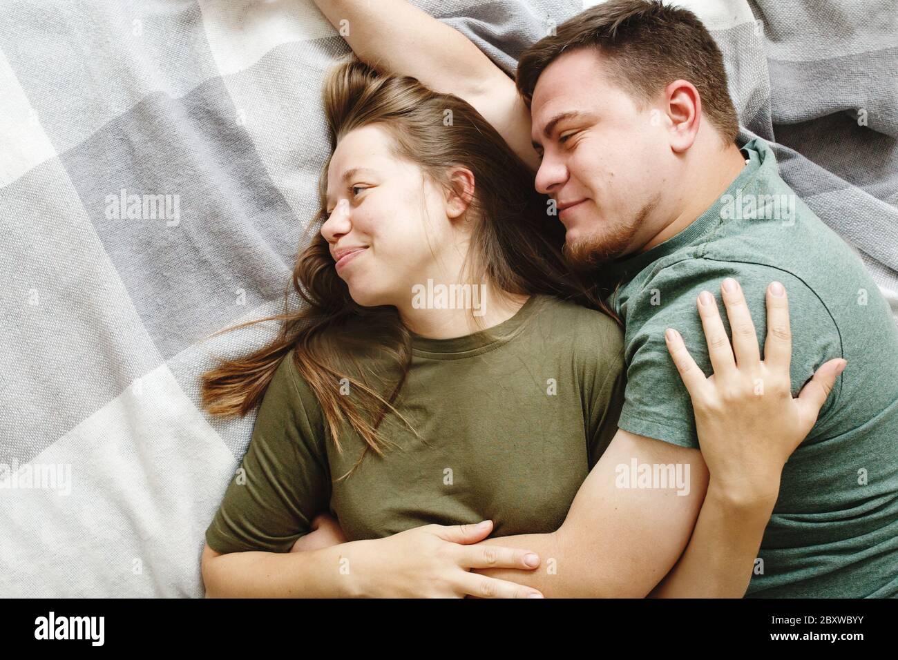 Porträt von liebevollen umarmenden Paar auf einem Bett zusammen liegen, bleiben zu Hause Konzept, Draufsicht. Junger Freund und Freundin, echte Menschen. Stockfoto