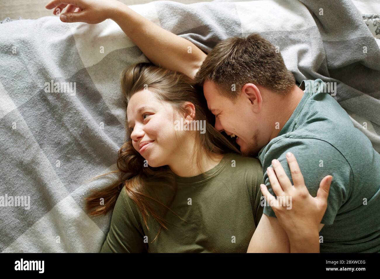 Portrait von lächelnd liebenden Paar auf einem Bett zusammen liegend, bleiben zu Hause Konzept, Draufsicht. Junge Freund und Freundin umarmen, echte Menschen. Stockfoto