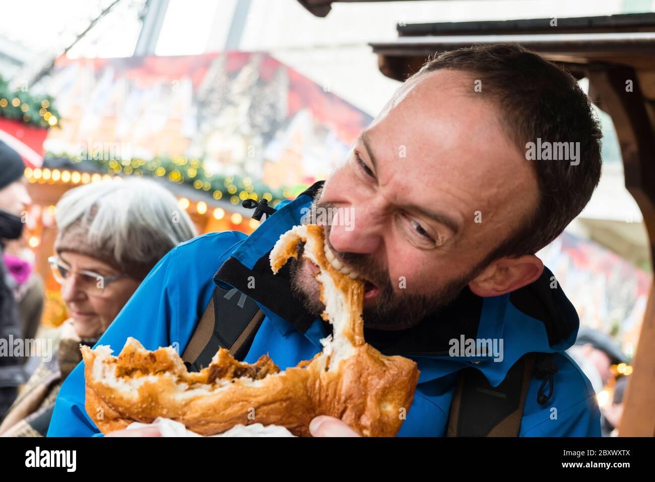 Männliche Touristen essen von einem Brotboot bis zu überfüllten Speisen von einem Outdoor-Food-Stand am Alexanderplatz Weihnachtsmarkt, Mitte, Berlin Stockfoto