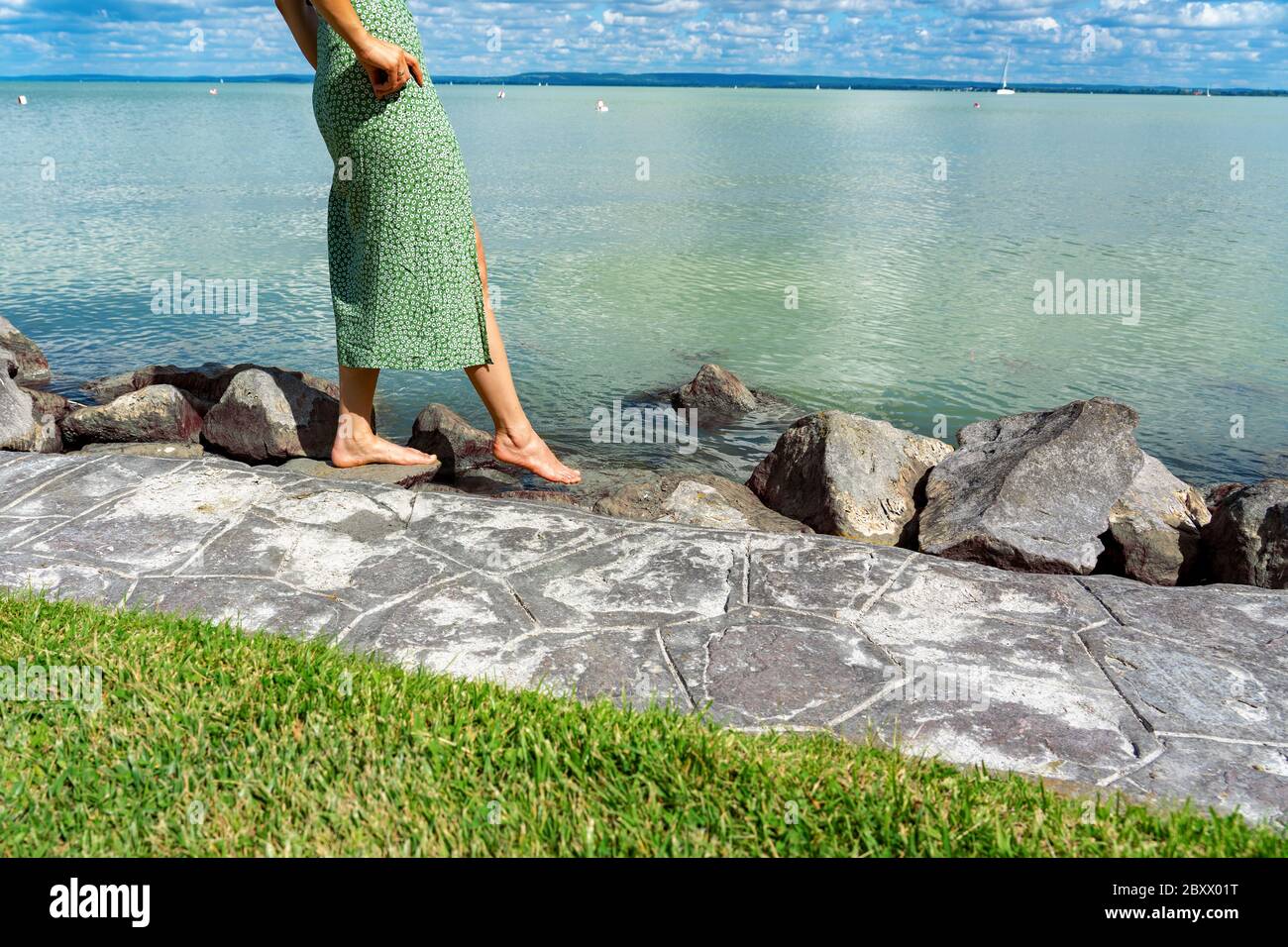 Frau versucht die Wassertemperatur mit ihren Füßen am Plattensee in Ungarn am Strand Badacsony mit blauem Himmel. Stockfoto