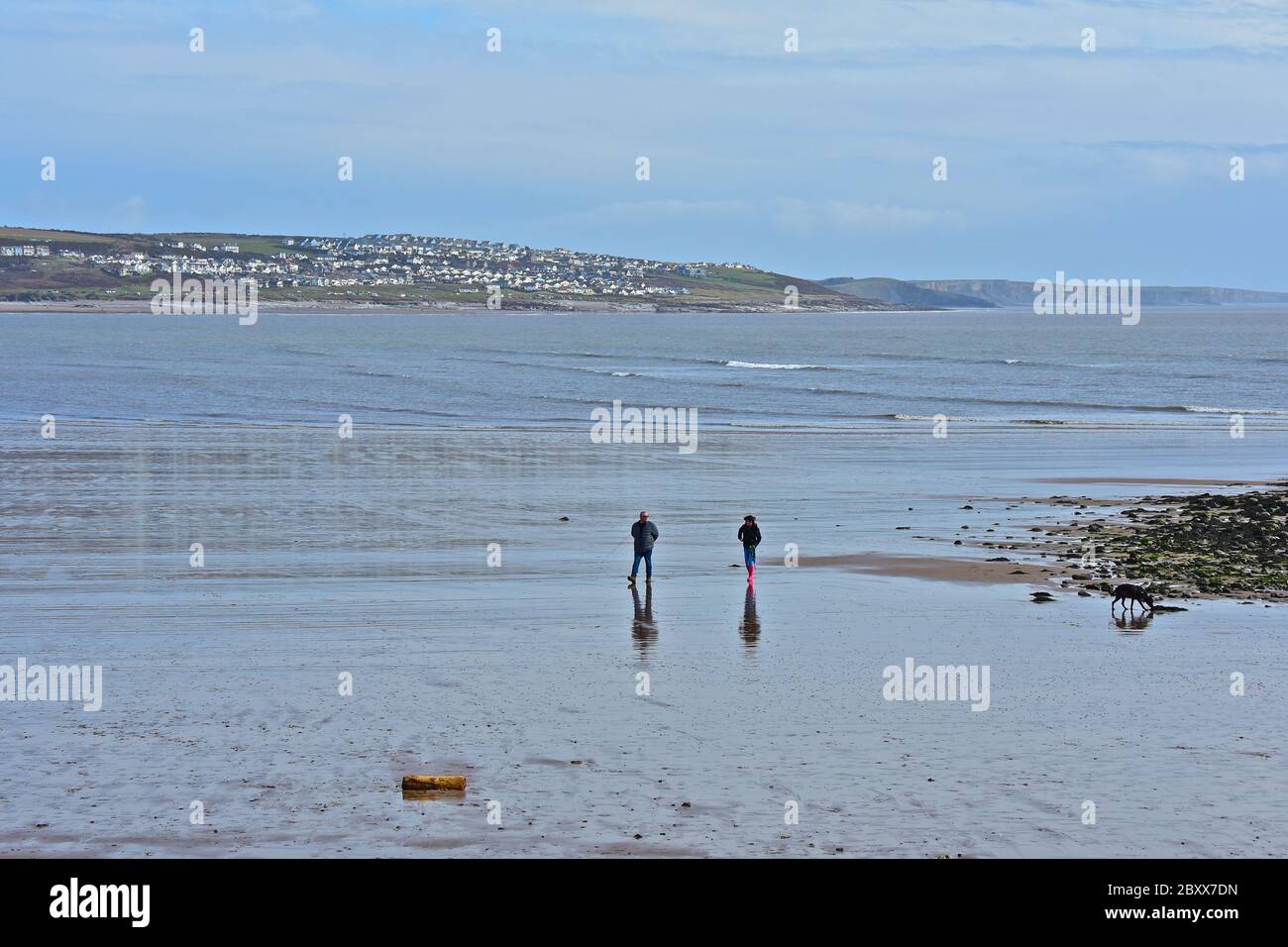 Fast menschenleeren Strand bei Porthcawl, mit Fernsicht auf Ogmore-by-Sea. Ein Paar mit ihrem Hund, am Wasser. Stockfoto