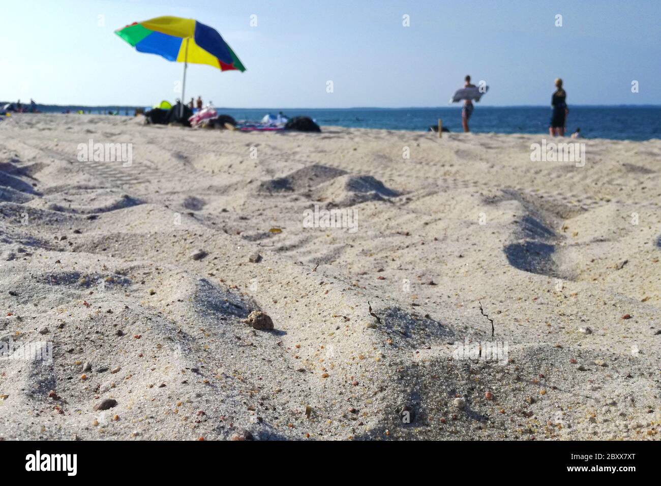 Sandstrand an der Ostsee mit Sonnenschirm und Wasser im Urlaub mit Sonne - Sonnenstrand mit Sand und Meer im Hintergrund verschwommene Menschen Stockfoto