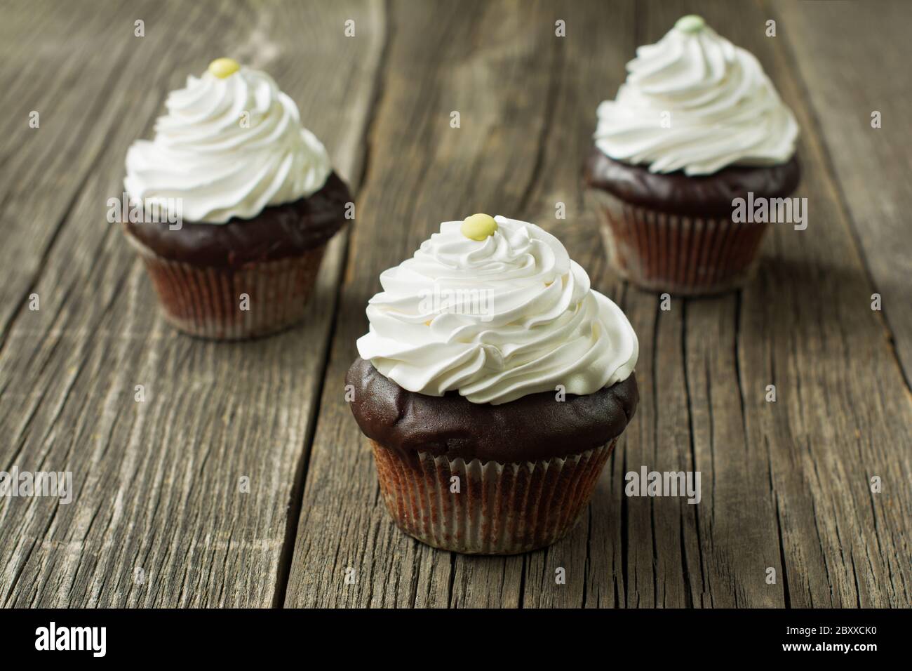 Hausgemachte Schokolade Cupcakes in Cupcake Liner, gekrönt mit Schlagsahne, verziert mit Knopf-förmigen Süßigkeiten, auf dem rustikalen Holzdiele Hintergrund. Stockfoto