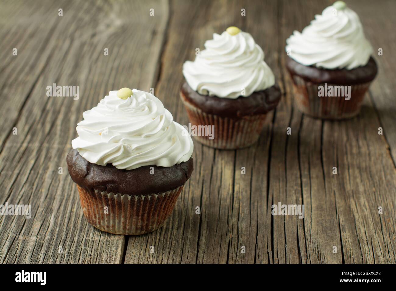 Schokolade Cupcakes in Papier Patty Fällen, gekrönt mit Schlagsahne und mit Knopf-förmigen Süßigkeiten, auf den rustikalen Holzplanken verziert. Stockfoto