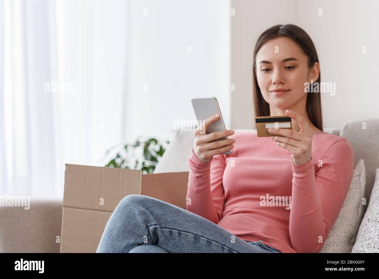 Schnelle Bestellung im Online-Shop. Mädchen mit Smartphone und Kreditkarte sitzt auf Sofa mit Pappkartons Stockfoto