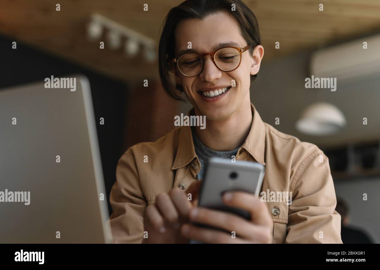 Glücklicher Mann mit Laptop-Computer, Handy, Suche nach Informationen mit mobilen App am Arbeitsplatz. Erfolgreiches Geschäft. Freiberuflicher Mitarbeiter, der von zu Hause aus arbeitet Stockfoto