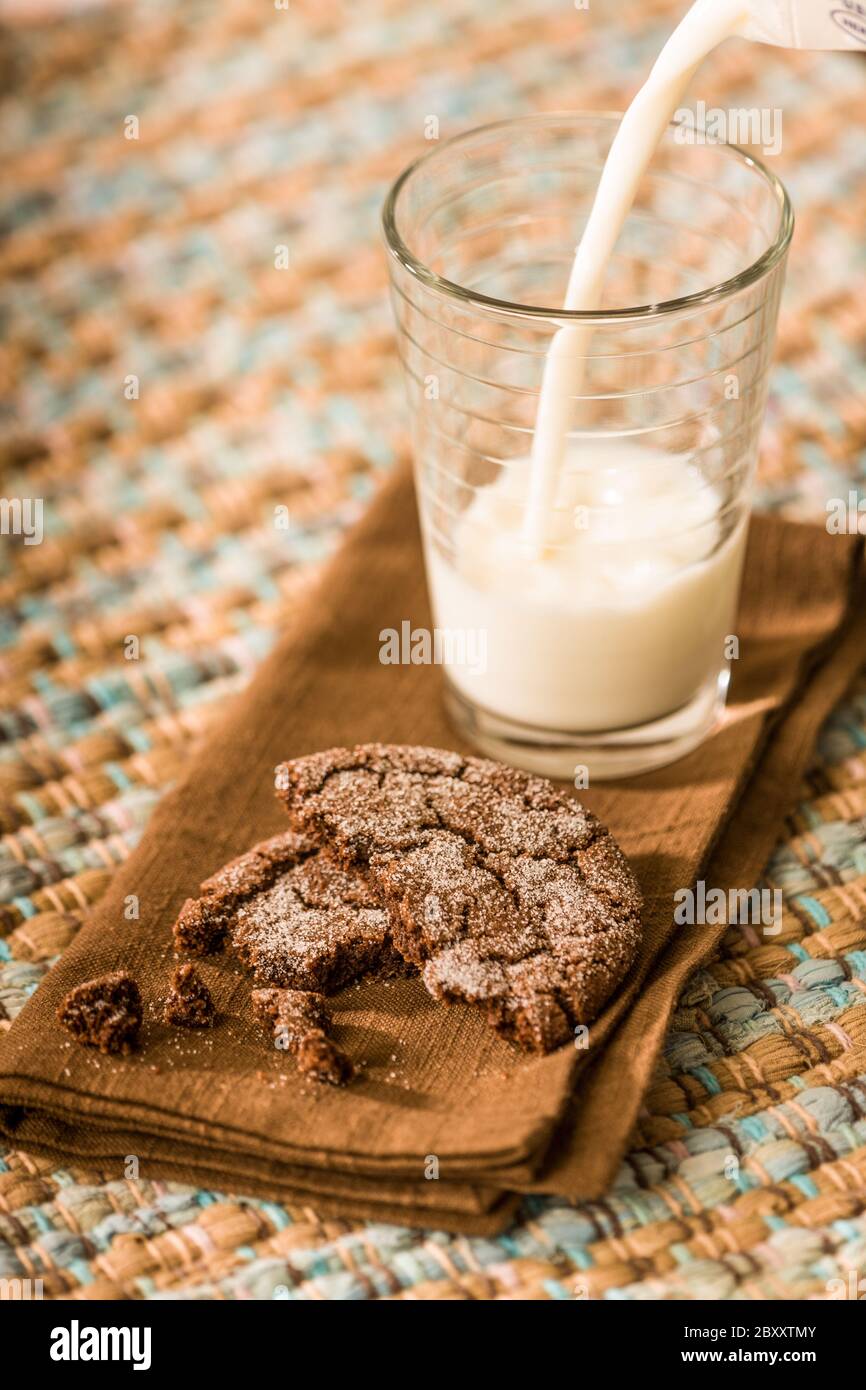 Teilweise verzehrtes hausgemachtes Schokoladenzuckerkekse und Milch, die in ein Glas gegossen wird Stockfoto