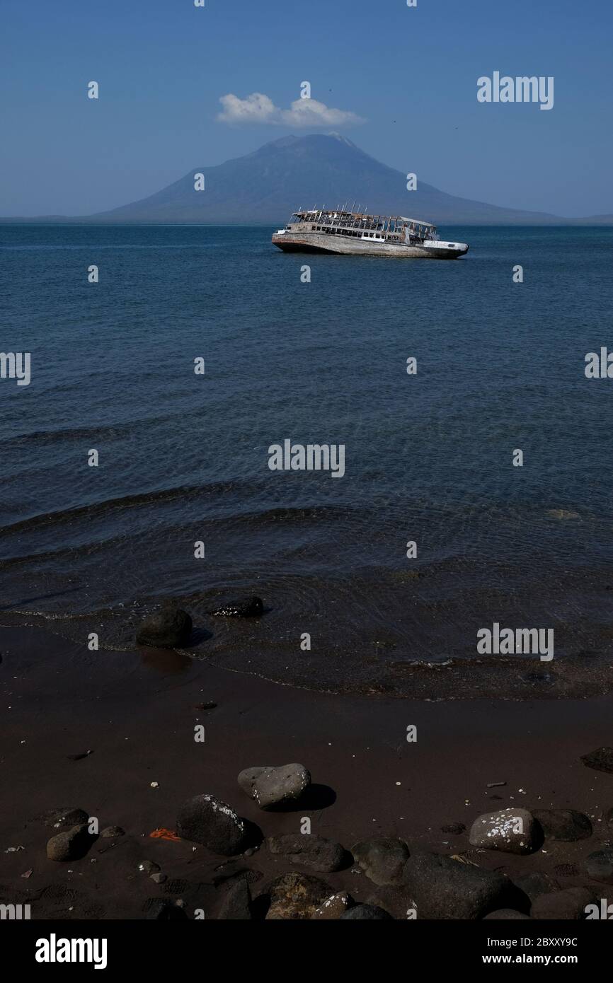Ein Blick aufs Meer vom Lewoleba Strand, der ein verlassene hölzerne Passagierschiff auf Küstenwasser und den Mount Lewotolok im Hintergrund zeigt. Stockfoto