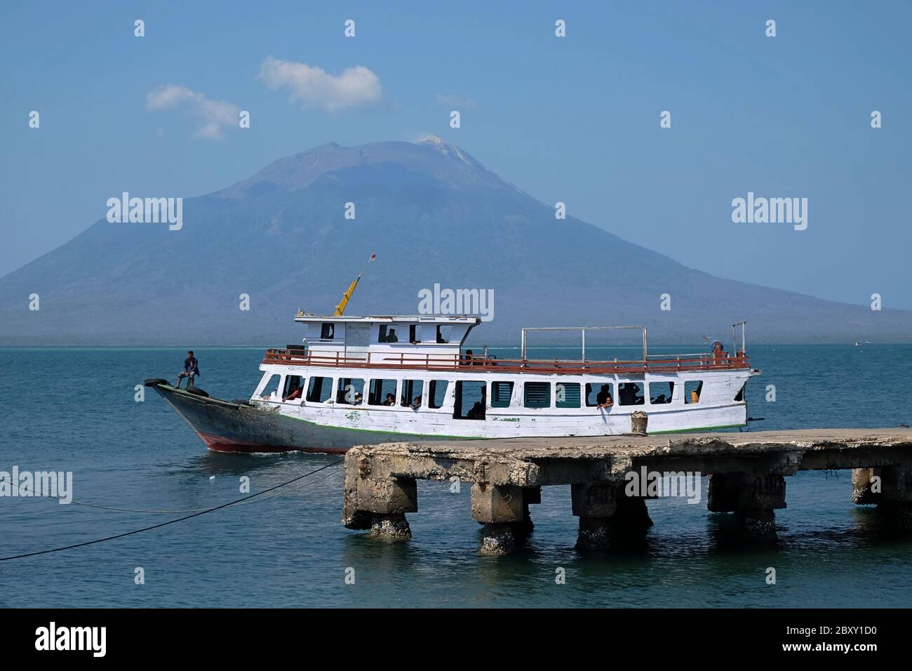 Im Hintergrund ist ein hölzernes Passagierschiff zu sehen, das sich auf dem Küstenwasser von Lewoleba bewegt, mit dem Lewotolok-Vulkan. Stockfoto