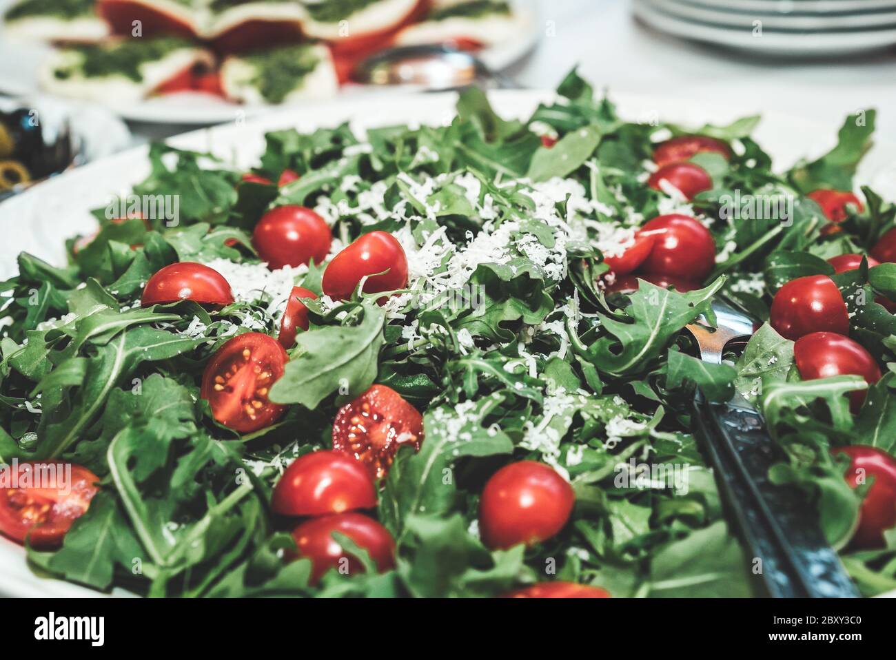 Frischer vegetarischer Salat mit Kirschtomate, Gartenrakete und geriebenem Käse auf dem Buffettisch. Feier, Party, Geburtstag oder Hochzeit Konzept. Stockfoto