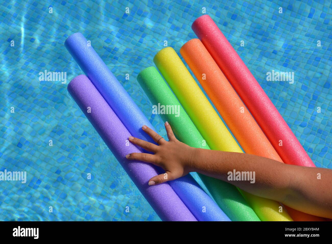 Frauenarm hält Poolnudeln in einer Regenbogenfarbsequenz in einem Schwimmbad zur Unterstützung von LGBTQ Pride Stockfoto