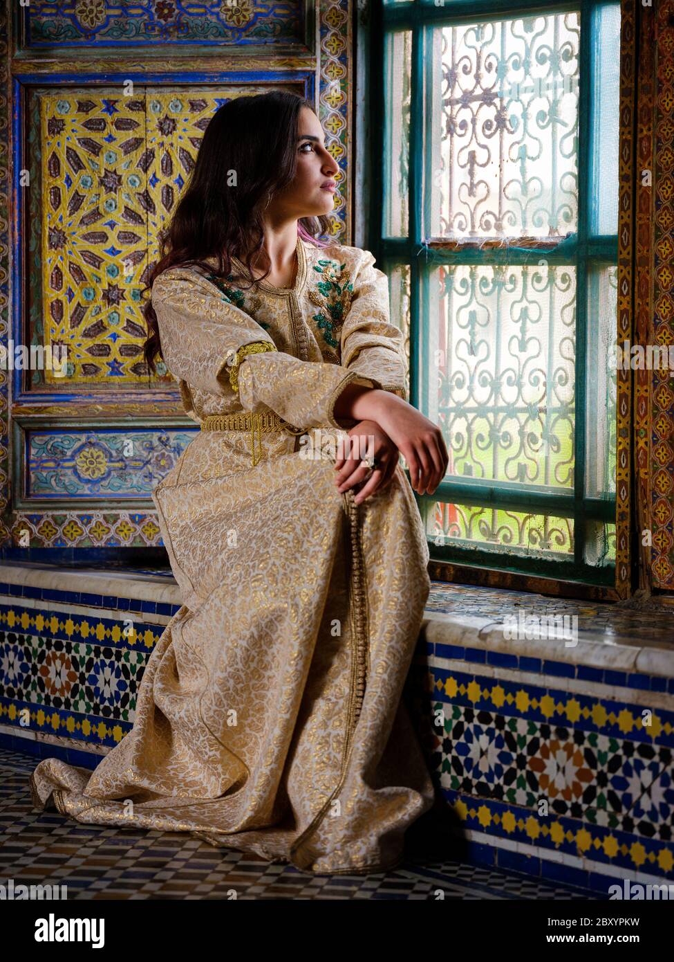FES, MAROKKO - UM MAI 2018: Junge Marokkanerin in traditioneller Kleidung, die in Fes. An einem Fenster sitzt Stockfoto