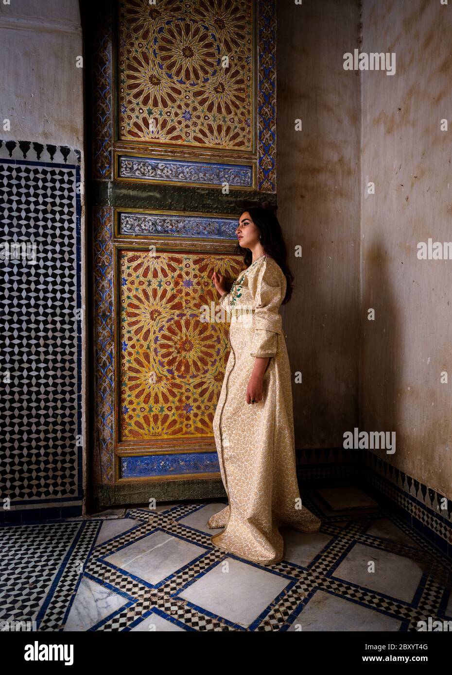 FES, MAROKKO - UM MAI 2018: Junge Marokkanerin in traditioneller Kleidung, die in Fes an einer marokkanischen Tür sitzt Stockfoto