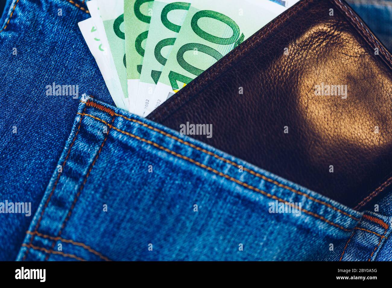 Braun Geldbörse mit Euros in die blauen Jeans Tasche. Wallet mit Euro-banknoten. Bargeld in der Brieftasche in der blauen Jeans Tasche. Euro Geld in Leder Stockfoto