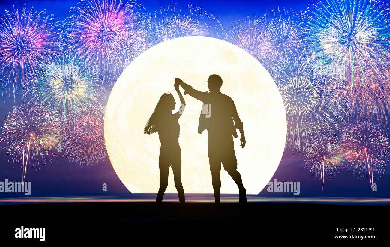 Ein romantisches junges Paar, das am Strand tanzt und das Feuerwerk beobachtet Stockfoto
