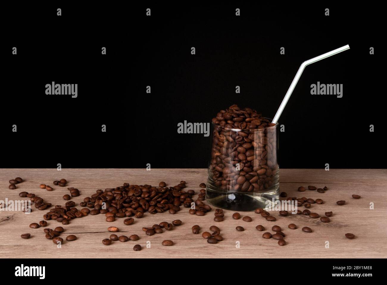 Whiskey-Glas voll gerösteten Kaffeebohnen mit Stroh auf einem Holzbrett vor dunklem Hintergrund stehend Stockfoto