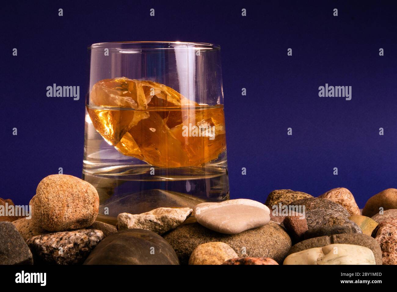 Glas mit Wasser und Bernstein im Inneren auf einem Haufen von Kieselsteinen stehen Stockfoto