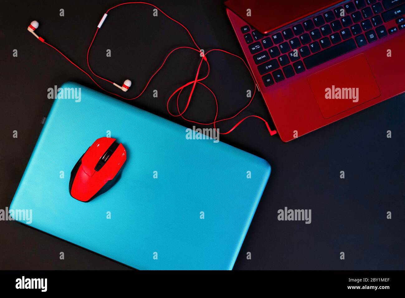 Draufsicht auf zwei farbige Laptops, türkis und rot, Kopfhörer und rote Computermaus auf dem blauen Stockfoto